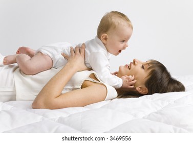 Young Mother With Baby Boy. Lying On Bed And Hugging. Face To Face, Side View