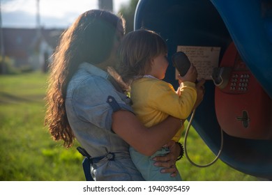 Young Mother And Baby Call On A Landline Street Phone In Telephone Booth In The Village In Summer. Walking With Family Summer Sunny Day In Sunshine. Artistic Focus