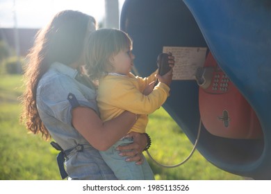 Young Mother And Baby Call On A Landline Street Phone In Telephone Booth In The Village In Summer. Walking With Family Summer Sunny Day In Sunshine. Artistic Focus