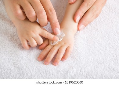 Young mother and baby fingers together applying moisturizing cream on baby hand on white towel. Care about children clean and soft body skin. Front view. Closeup. 