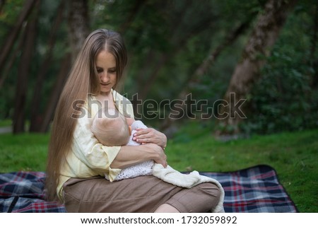 Young mother breast-feeding newborn in Park. Mother and baby sitting on picnic blanket.