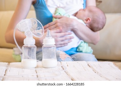 A young mother breastfeeds her baby and an electric breast pump is standing in front of her on a wooden table
