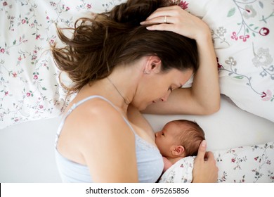 Young mother breastfeeds her baby, holding him in her arms and smiling from happiness