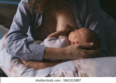 Young mother breastfeeds her newborn at home. Low key dark cozy. Caring togetherness motherhood. Security silence. Innocent. Lactation. Life style small moments real life