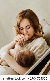 Young mother breastfeeds her newborn on a cloth background in the studio.