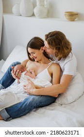 A young mother breastfeeds a newborn girl sitting next to her husband.
