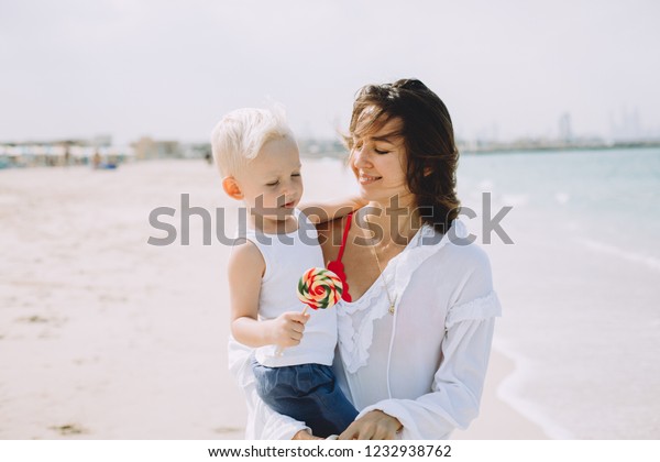 Young mother carring her little son at sandy beach in\
Dubai, UAE