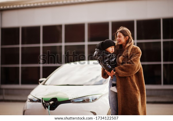 Young mother with child charging electro car at\
the electric gas station.