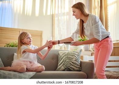 Young Mother With Child Daughter At Home On The Couch Drinking Milk And Cookies, Laughing And Talking Together