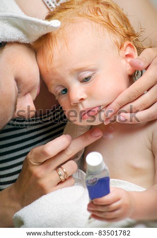 Young mother with cute little baby after bath using cream