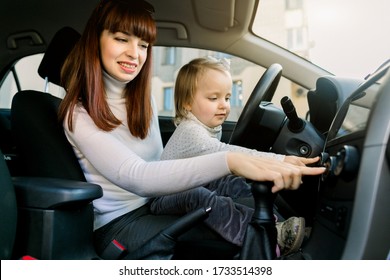 Young Mother With Cute Little Girl Child Playing In The Car, Listening To Music Or Radio, Sitting Together In The Front Seat Near Car Steering Wheel. Family Trip, Child In A Car