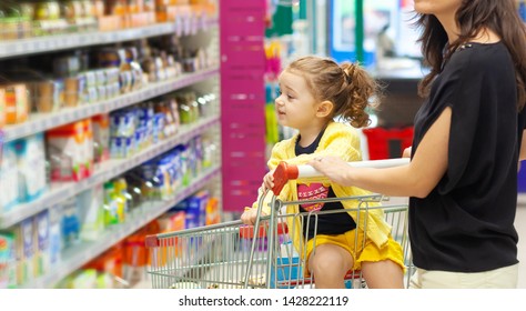 Young Mother and daughter in the cart shopping for groceries in supermarket.