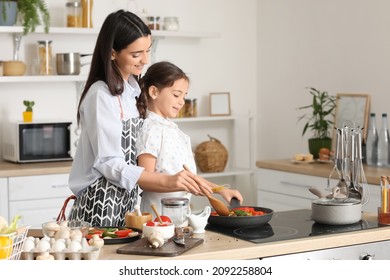 Young mother and daughter cooking together in kitchen at home