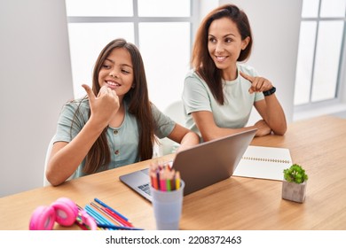 Young Mother And Daughter Doing Homework At Home Pointing Thumb Up To The Side Smiling Happy With Open Mouth 