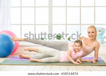 Young mother and daughter exercise together indoors