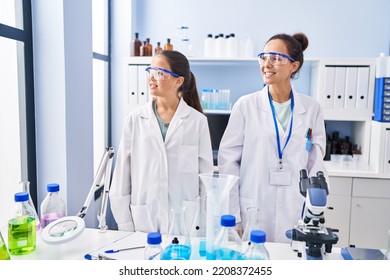 Young Mother And Daughter At Scientist Laboratory Looking Away To Side With Smile On Face, Natural Expression. Laughing Confident. 