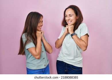 Young Mother And Daughter Standing Over Pink Background Laughing Nervous And Excited With Hands On Chin Looking To The Side 