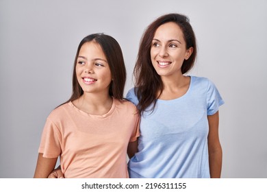 Young Mother And Daughter Standing Over White Background Looking Away To Side With Smile On Face, Natural Expression. Laughing Confident. 