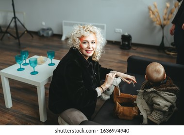 Young Mother Dressing Up Her Son In Winter Clothes Before Going Out. Parenting, Taking Care Of Child Concept.