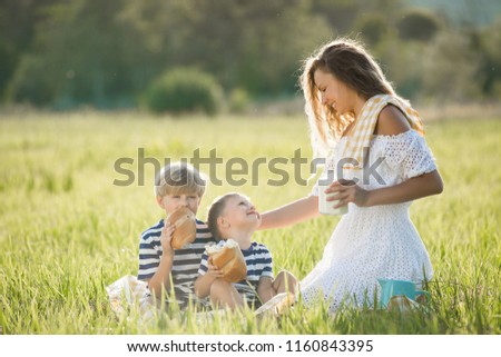 Young mother drinking organic fresh milk with her children outdoors