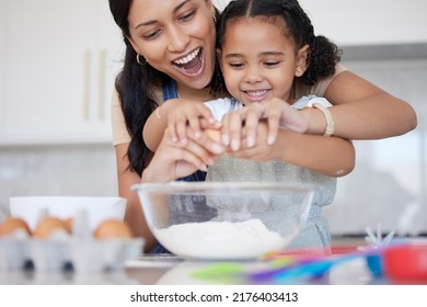 Young Mother Enjoying Baking, Bonding With Her Little Daughter In The Kitchen At Home. Little Latino Girl Smiling While Helping Her Mother Cook A Meal At Home. Child Cracking An Egg For A Recipe