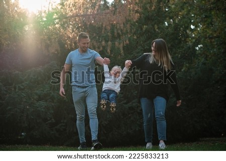 Young mother and father are having fun with child while walking with holding hands together in the autumn park concept of happy family.