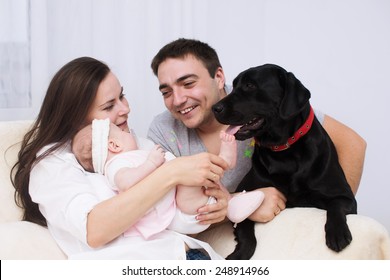 Young Mother And Father With Newborn Baby Playing With Dog