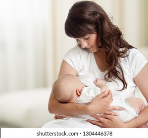 Young mother feeding breast her newborn baby at home in white room