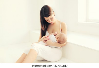 Young mother feeding breast her baby at home in white room near window