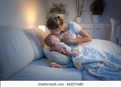 Young Mother Feeding Her Baby From Bottle In Bed At Night