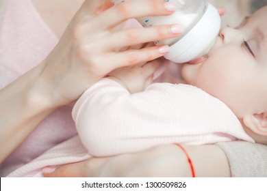 Young Mother Feeding Her Little Cute Baby Daughter With Bottle Of Child Formula. Woman With Her Newborn Baby At Home. Mom Taking Care Of A Child. Alternative To Breast Feeding. 