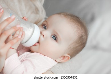 Young Mother Feeding Her Little Cute Baby Daughter With Bottle Of Child Formula. Woman With Her Newborn Baby At Home. Mom Taking Care Of A Child. Alternative To Breast Feeding. 