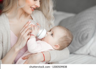 Young Mother Feeding Her Little Cute Baby Daughter With Bottle Of Child Formula. Woman With Her Newborn Baby At Home. Mom Taking Care Of A Child. Alternative To Breast Feeding. 