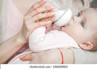 Young Mother Feeding Her Little Cute Baby Daughter With Bottle Of Child Formula. Woman With Her Newborn Baby At Home. Mom Taking Care Of A Child. Alternative To Breast Feeding. 