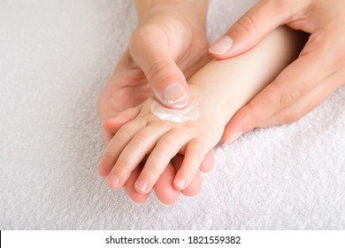 Young Mother Finger Applying Moisturizing Cream On Baby Hand On White Towel. Care About Children Clean And Soft Body Skin. Closeup.