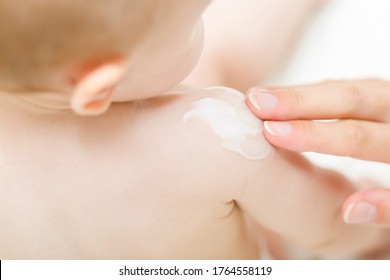 Young mother fingers applying white moisturizing cream on baby shoulder. Care about children clean and soft body skin. Closeup. 