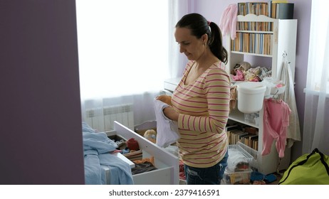 Young mother folding clothes near the dresser by her cute baby playing on the floor - Powered by Shutterstock