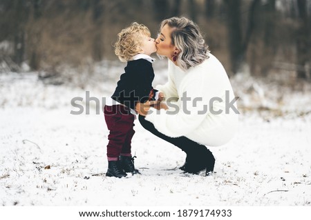 A young mother giving her son a kiss on the lips outdoors on a winter day