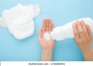 Young Mother Hand Holding White Bottle And Pouring Talcum Powder On Palm. Baby Skin Protection Before Diaper Changing. Light Blue Table Background. Pastel Color. Closeup. Point Of View Shot. 