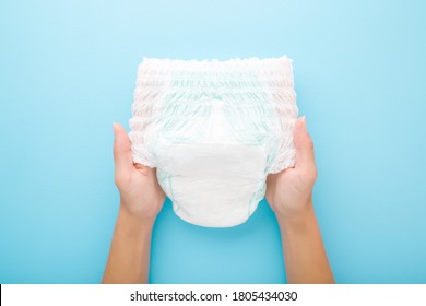Young mother hands holding white baby diaper pants on light blue table background. Pastel color. Closeup. Point of view shot.