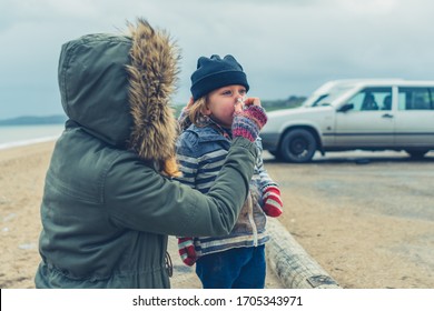 A Young Mother Is Helping Her Preschooler Blow His Nose In A Car Park By The Beach In Winter