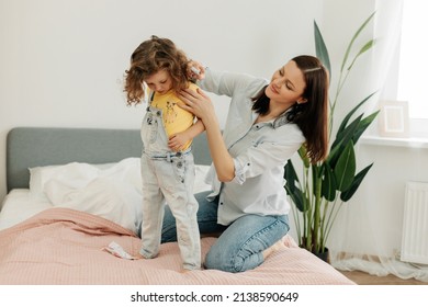 A Young Mother Helps Her Little Daughter To Change Clothes. Taking Care Of Children, Help, Motherhood