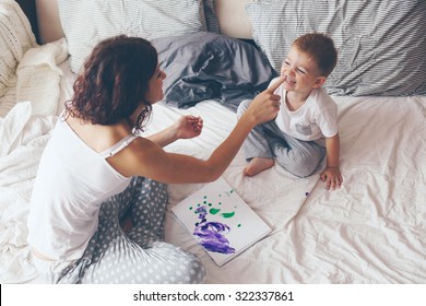 Young mother and her 2 years old little son dressed in pajamas are relaxing   playing in the bed at the weekend together  lazy morning  warm   cozy scene  Pastel colors  selective focus 