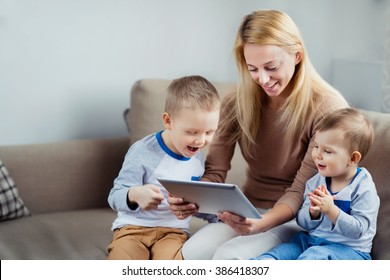 Young mother with her 2 years old little son and 5 years old son playing with digital tablet at home