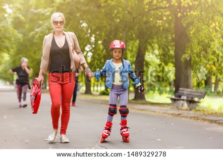 Young mother with her 5 years old daughter rollerskating in park