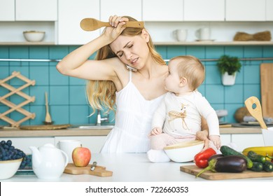 Young mother with her baby daughter in a modern kitchen setting. Young attractive cook woman desperate in stress, tired. 