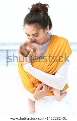 Young mother with her baby in sling walking outdoors