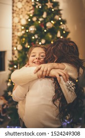 Young Mother And Her Cute Little Daughter Are Having Hug And Enjoy Beside Christmas Tree At The Home. 