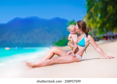 Young mother and her cute little baby running and playing on a beautiful tropical beach enjoying family summer holiday