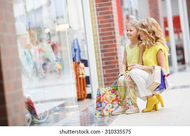 Young Mother And Her Daughter Doing Shopping Together. Woman With Child On Shopping In Shopping Mall With Bags. Woman With Child Having Fun And Enjoying Shopping Time